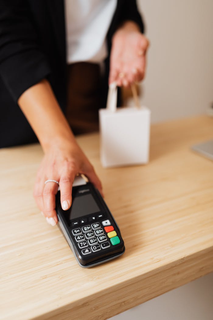 Hand making a contactless payment with a terminal on a wooden retail counter.