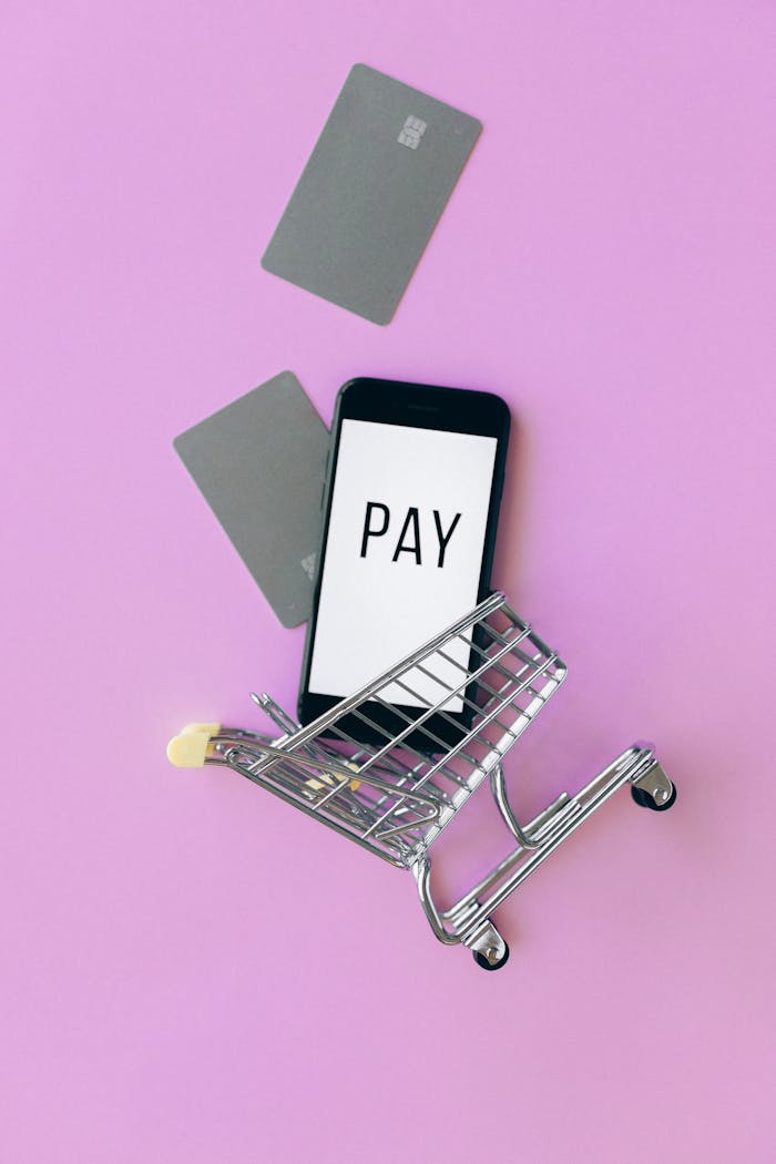 Top view of a smartphone in a shopping cart with credit cards on a purple background.
